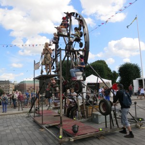 Ferris wheel at children's carnival with a parent cranking the wheel on the right.